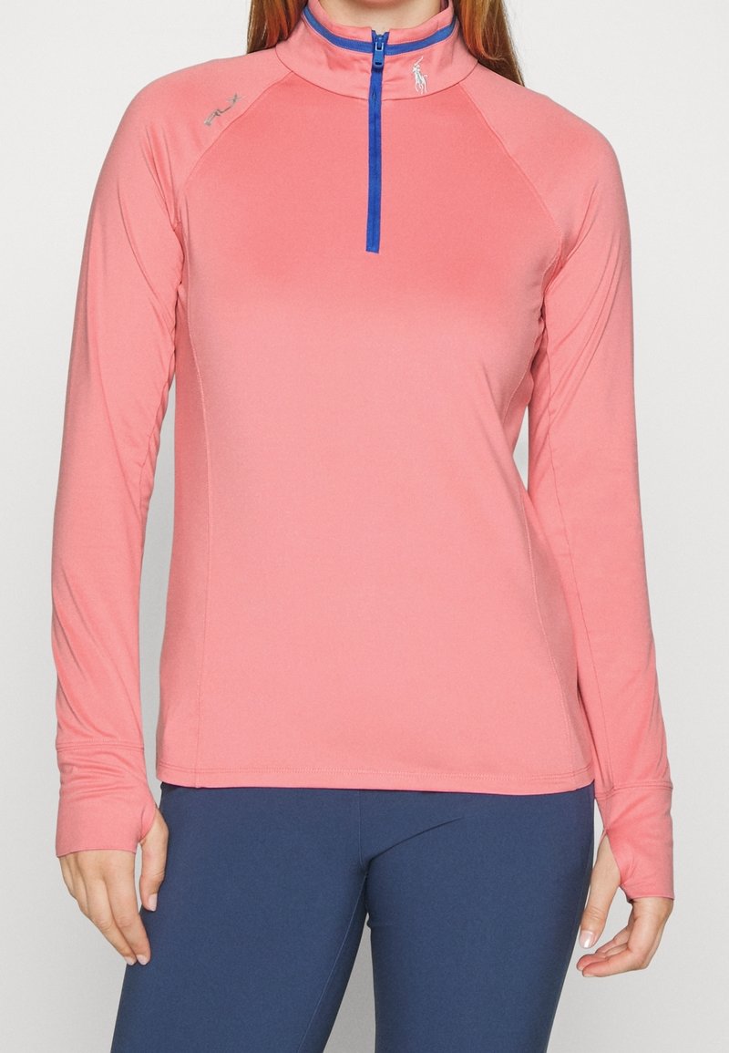 Dlouhý rukáv sportovní top v korálové barvě s půlzipem a modrým zipem. Obsahuje raglánové rukávy a hladký, elastický materiál.