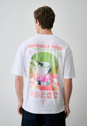 Bărbat purtând tricou alb care arată o grafică colorată a unui cocktail japonez yuzu cu text și design floral pe spate.