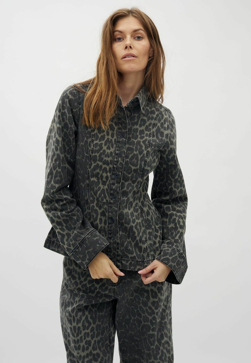 Schwarze Jeansjacke mit grünem Leopardenmuster, mit Knopfverschluss, spitzem Kragen und langen Ärmeln. Strukturiertes Gewebe mit Akzenten in der Naht.