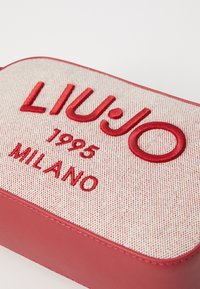Crvena kožna i tkaninska torba s vezom "LIUJO 1995 MILANO", sa strukturiranim, pravokutnim oblikom i detaljima od šivanja.