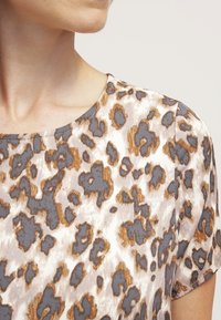 Top con stampa leopardata e scollatura rotonda, caratterizzato da motivi beige, marroni e grigi su un tessuto morbido. Maniche corte e superficie liscia.