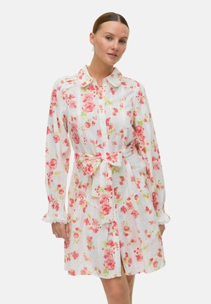 Blommig klänning i lätt tyg med rosa och gröna blommor på vit bakgrund, med krage och bälte runt midjan.