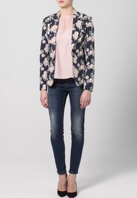 Sako s květinovým vzorem navy barvy se strukturovanými klopami, spárované s světle růžovým topem, tmavými skinny džíny a černými podpatky.