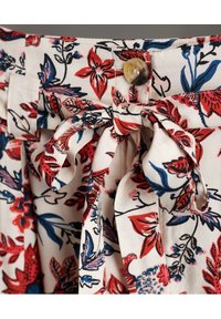 Tela con estampado floral de flores rojas y azules sobre un fondo crema. Cuenta con un cinturón para anudar y un detalle decorativo de botón.