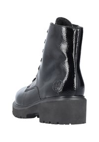 Bottes noires à la cheville avec une finition en cuir verni brillant, dotées d'une semelle robuste, d'un design à lacets et d'un logo circulaire sur le côté extérieur.