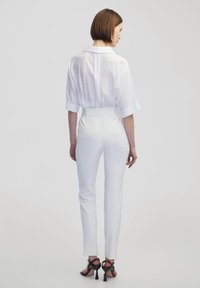 Witte kortarmige overhemd met kraag, gecombineerd met strakke witte broek en zwarte sandalen met hak. Soepele textuur, slanke silhouet.