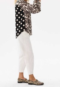Blusa a fantasia con pois neri e motivo paisley beige; pantaloni bianchi a vita alta; e ballerine multicolori con stampa serpente e tacco basso.