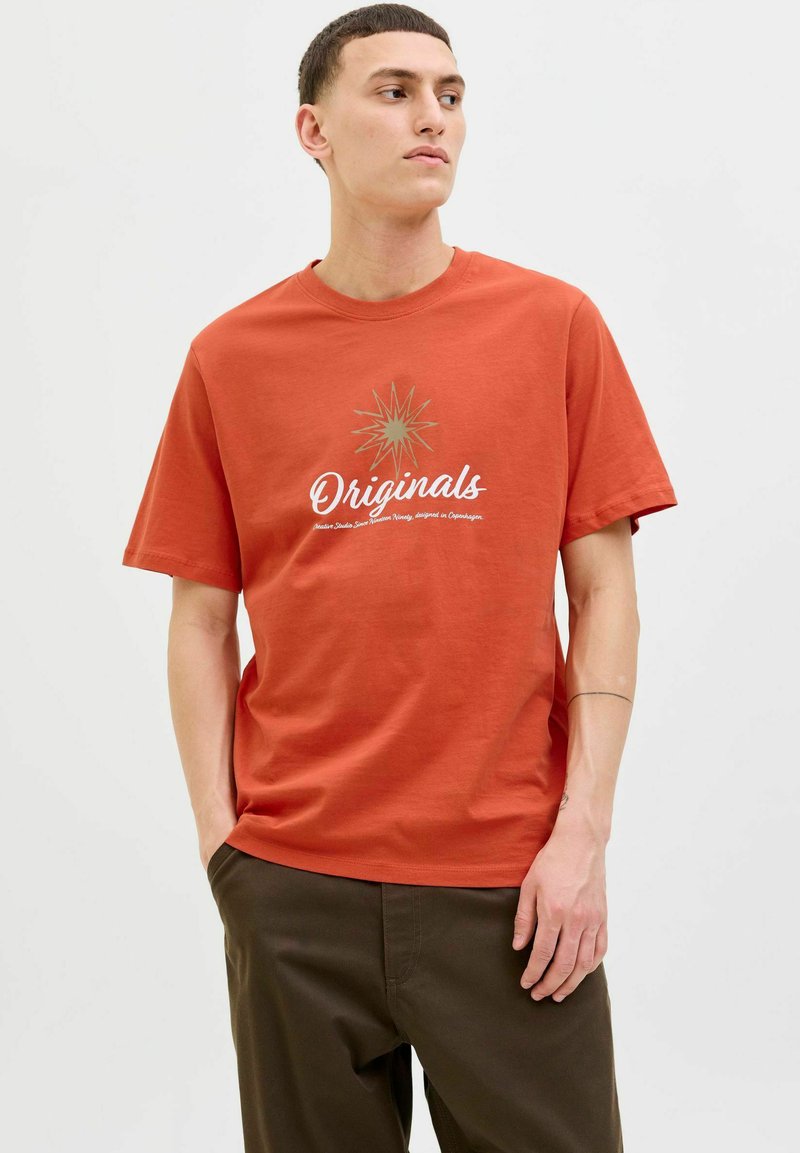 Rust-orange bomulds t-shirt med et hvidt script "Originals" logo og en gylden stjernespænde grafik, afslappet pasform, korte ærmer.