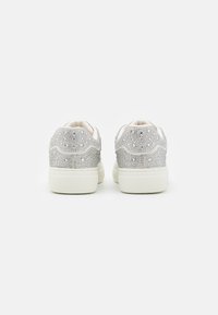 White sneakers with silver rhinestone details on the heel, textured upper, and a smooth sole. Rounded shape with lace-up design.