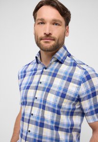 Camicia a maniche corte a quadri in blu, bianco e giallo. Presenta un colletto button-down e bottoni a contrasto, con diversi modelli di quadri.