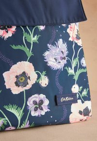 Laivyno mėlynumo gėlėta medžiaga su rožinėmis ir violetinėmis gėlėmis bei žaliomis lapelėmis, papuošta baltai siuvinėta "Cath Kidston" etikete.
