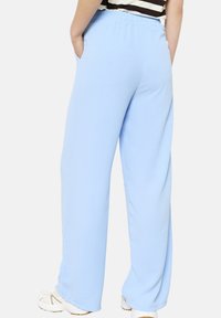 Pantalones de pierna ancha en azul claro, confeccionados con tela suave, cuentan con una cintura elástica y bolsillos laterales. Llevados con una blusa a rayas y zapatillas.