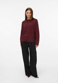 Burgundy stickad tröja med rund halsringning och långa ärmar, i kombination med svarta vida byxor och spetsiga svarta klackar.