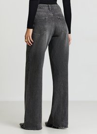 Pantaloni in denim nero a gamba larga con orlo sfrangiato, caratterizzati da una vita aderente, tasche posteriori e una texture sbiadita.