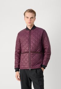 Quilted, maroon jacket with a zip front, black collar, and brown accent belt at the waist. Features ribbed cuffs and smooth texture.