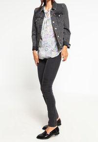 Giacca di denim nera con bottoni argentati, blusa leggera a fantasia, jeans skinny neri e mocassini neri lucidi. Design semplice e forma aderente.