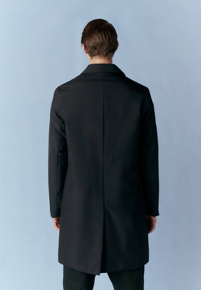Sort frakke med en figursyet design og lange ærmer, der har en notch-krave og en split bagpå. Glat tekstur mod en lyseblå baggrund.