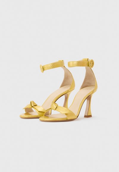 Κίτρινες σανδάλια με ψηλά τακούνια, λουριά στον αστράγαλο και ανοιχτά δάχτυλα, με υφασμένο μοτίβο και έναν κόμπο στα μπροστινά λουριά.