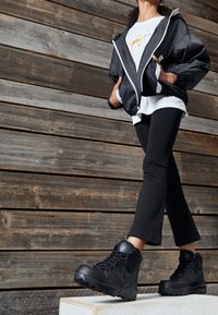 Black zip-up jacket with white accents, layered over a white shirt with a colorful graphic, paired with black flared leggings and black boots.