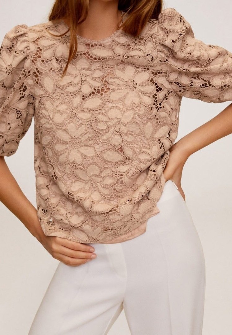 Vaaleanbeige pitsipaita, jossa on liehukkeet ja kukkakuviot sekä teksturoitu muotoilu. Yhdistetty valkoisiin housuihin.