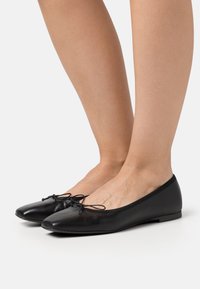 Schwarze Leder-Ballerinas mit runder Zehenpartie, elastischem Besatz und einer Schleifenakzentuierung vorne. Glatte Textur und minimalistisches Design.
