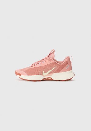 Pink Nike trail running shoe with white swoosh logo, textured sole, and lace-up design on a light gray background.