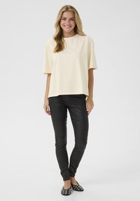 Lys gul kortærmet top med subtile pynt, parret med sorte strukturerede leggings og sorte slip-on sko med nitter.