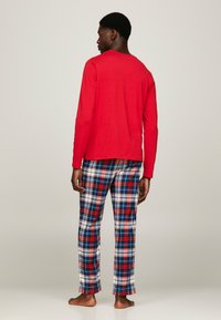 Maglietta rossa a maniche lunghe e pantaloni da pigiama a quadri blu con colori rosso, bianco e blu. Realizzati in cotone con una vestibilità comoda.