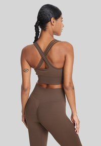 Brązowy zestaw sportowy, składający się z crop topu z krzyżującymi się ramiączkami oraz dopasowanych legginsów z wysokim stanem, wykonany z teksturowanej, elastycznej tkaniny.