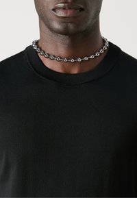 Black ribbed knitted sweater with a crew neckline, worn with a choker of silver spherical beads, resting just above the collarbone.
