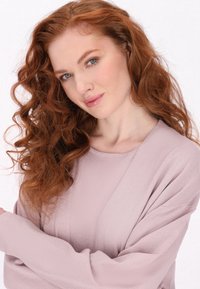 Šviesiai rožinė megztinis su ilgomis rankovėmis ir laisvu siluetu. Audinys turi švelnų blizgesį, tekstūruotą paviršių su vertikaliomis juostelėmis ir plačiu iškirpimu.