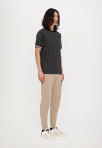 Svart mønstret t-skjorte med korte ermer, beige joggebukser og hvite joggesko. Materialet virker mykt med kontrastdetaljer.