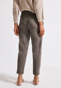 Pantaloni grigi a sigaretta con cintura elastica e due tasche posteriori, abbinati a un top in pizzo color beige chiaro e sandali nudi con cinturino.