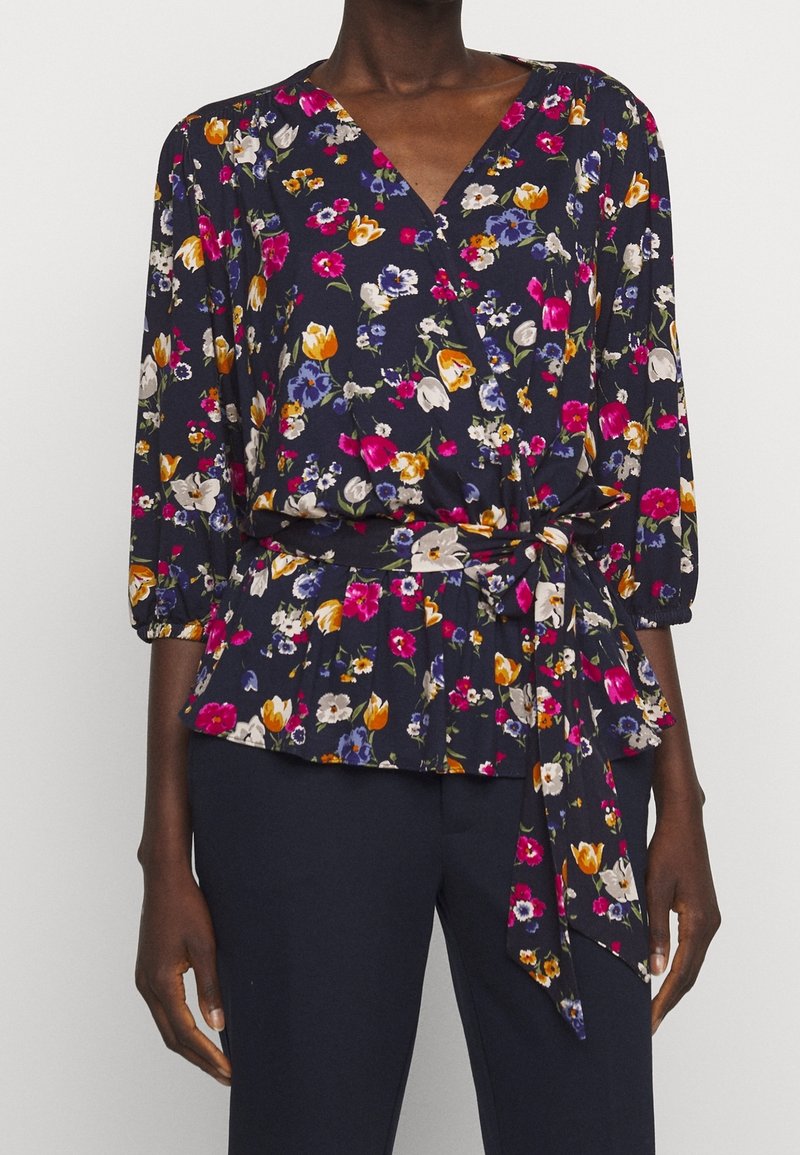 Blusa avvolgente floreale con sfondo blu navy, maniche 3/4, cintura a peplo con cintura annodata e una varietà di motivi floreali colorati.