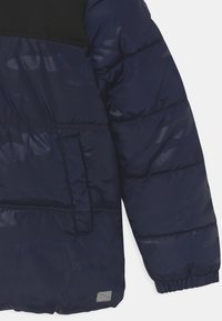 Námořnická modrá prošívaná bunda se sakem a kapsami s elastickým manžetem a jemným maskovacím vzorem na bílém pozadí.