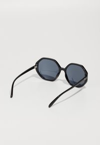 Ochelari de soare octagonali negri cu lentile gri închis. Rame din plastic lucios și brațe elegante. Design simplu, fără modele sau accente suplimentare.