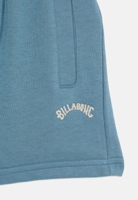 Modré bavlněné šortky s jemnou texturou, bočními kapsami a vyšitým nápisem "BILLABONG" v bílé barvě pod lemem.