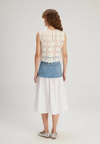 Haut en dentelle blanche avec des motifs floraux, associé à une jupe en denim et un tissu blanc fluide. Des chaussures plates argentées complètent le look.
