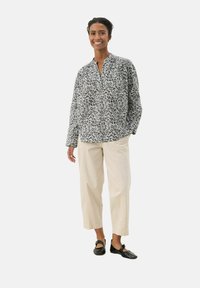 Blusa a maniche lunghe bianca e nera a motivo a V, abbinata a pantaloni morbidi color crema e scarpe nere.