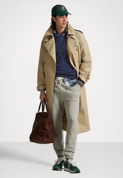 Beige trenchcoat, marinblå sweatshirt, rutig skjorta, gråa mjukisbyxor, gröna sneakers, mörkbrun läderväska, handledsur med silverdetaljer.