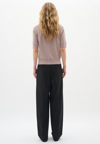 Kurzärmliger, hellmaulbeerfarbener Pullover, kombiniert mit hochgeschnallten, weit geschnittenen schwarzen Hosen. Der Pullover hat einen figurbetonten Saum und eine glatte Textur.