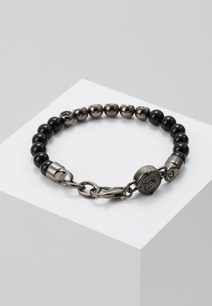 Bracelet avec des perles rondes noires alternées et des perles métalliques irrégulières, avec un fermoir mousqueton et un charm décoratif rond.