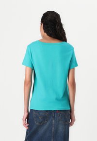 Turkise kortærmet t-shirt med bred halsudskæring, glat bomuldsstruktur, parret med en denimnederdel, der viser diskrete syninger.