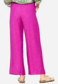 Pantaloni larghi fucsia realizzati in tessuto leggero, con una vestibilità rilassata e una cintura elastica. Sandali piatti in evidenza.