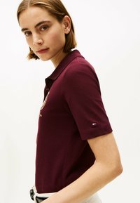 Mørkerød polo t-shirt med korteærmer, med krave og broderet logo på brystet. Accentueret af et lille flagdetalje på ærmet.