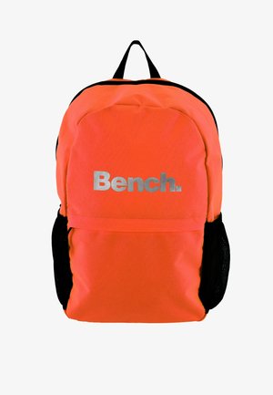 Pomarančna tkaninska nahrbtnik z črnimi detajli, ki ima sprednjo žepek in srebrni logo "Bench." spredaj. Nastavljive naramnice.
