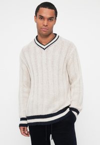 Crèmekleurig gebreid sweater met een V-hals, ribbelstructuur en marineblauwe strepen accenten bij de kraag en de zoom. Ontspannen pasvorm.