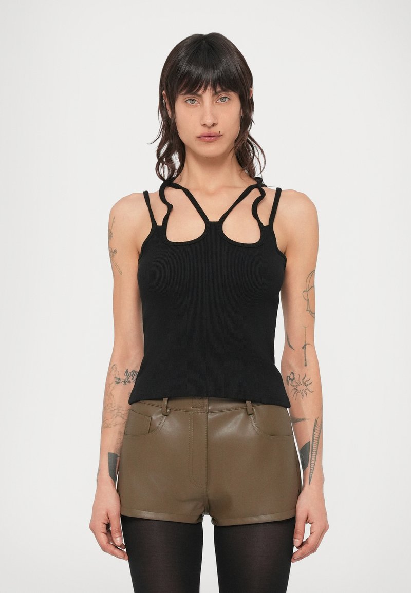 Top preto canelado com recortes únicos no decote e alças finas. Combinado com calções verde-oliva, mostrando uma silhueta justa.