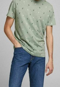 Groene T-shirt van zachte stof, met kleine bedrukte ananassen in het wit en marineblauw. Gepaard met blauwe spijkerbroek, op maat gesneden.