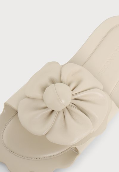 Sandale beige à enfiler avec une grande fleur en cuir souple sur le dessus et des bords festonnés sur la semelle.